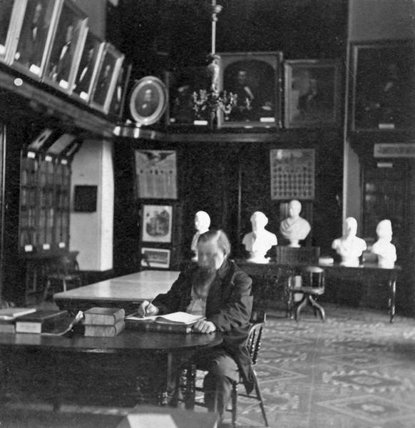 Librarian Daniel S. Durrie seated in the two-story high gallery that the Historical Society occupied in the old South Wing of the Wisconsin State Capitol from 1866 until 1883. In addition to this room, the Society also filled the entire second floor of the South Wing — the same floor with the Senate and the Assembly. Dating to approximately 1880, this photograph is one of a very few that document the early appearance of the Third Capitol. Of note is the patterned carpet and table. The photograph also documents the prominent role of the Society's painting and art collection.