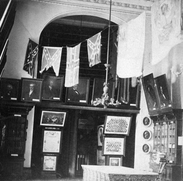 A two-story gallery of the Historical Society in the Wisconsin State Capitol, with captured Confederate army flags on display. This photograph was taken in the old South Wing rooms into which the Society moved in 1866. Because of its expanding collections, in 1883 the Society moved to the new South Wing addition. It is likely that decorative treatment of this room, which was photographed about 1880, documents something of the appearance of the Third Capitol as originally constructed.