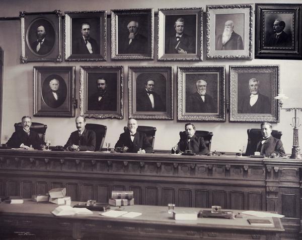 Group portrait of the Wisconsin Supreme Court in 1903, the year in which a constitutional amendment approved expansion of the court from five to seven judges. Seen here (left to right) are Joshua E. Dodge, John B. Winslow, John B. Cassoday, Rouet D. Marshall, and Robert G. Siebecker. The portraits of former justices hang on the wall behind them. The Supreme Court chamber was located in the addition to the North Wing constructed in 1883.