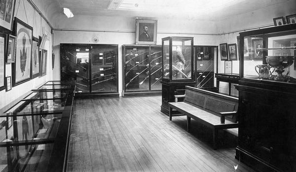 The Civil War Room of the Historical Society Museum photographed sometime after 1900 when the society moved from third Wisconsin State Capitol to its new building on State Street. Old Abe, Wisconsin's war eagle, is on display, stuffed, in a glass case. This photograph can be dated as prior to April, 1903 because at that time Governor Robert La Follette ordered Old Abe returned to the new G.A.R. Museum in the Capitol. As a result, Old Abe became one of the objects destroyed in the Capitol fire of 1904.