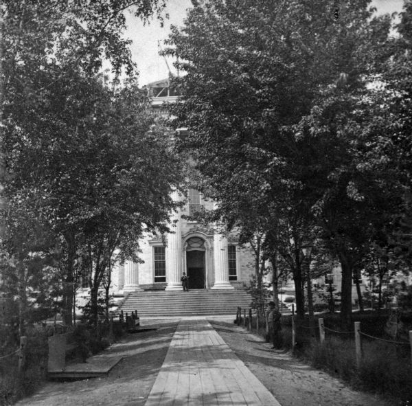 The entrance to the third Wisconsin State Capitol before the construction of the dome, showing the park and walkway. Framing for the dome can be seen through the trees. Because this entrance faced King Street, then Madison's leading commercial street, this would have been regarded as the front door of the Wisconsin State Capitol.
