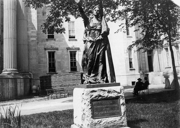 Only the salvaged planking behind the "Forward" statue created by Jean Pond Miner indicates that anything more is going on in this picture than a peaceful summer afternoon in Madison's Capitol Park.  In fact, demolition of the fire-ravaged Third Capitol is well underway.  The North Wing, behind the two ladies with their parasols, was the only portion of the Capitol that escaped damage and it continued to be used for several years. The octagon tower, behind the two men on the bench, marked the extent of the original building completed in 1869 and the point at which the fire was halted in 1904.