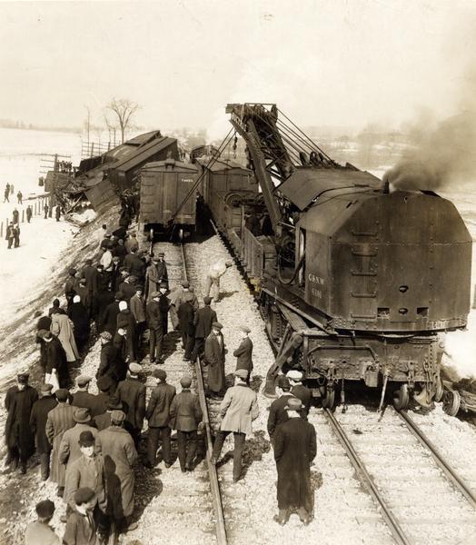 Elevated view of the wreck of a Chicago and Northwestern Railroad train at Corliss. A large crowd of men are watching as a Bucyrus crane is lifting a car back onto the tracks. Sturtevant was originally Corliss, but was changed in 1901.