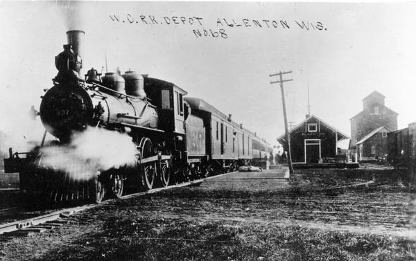 Wisconsin Central Railway locomotive No. 207 and train No. 6 and the depot. The locomotive was built by the Brooks Locomotive Works in 1890, and scrapped in 1916. The engineer was George W. Martin, father of railroad historian Roy L. Martin, from whose collection this image originates.