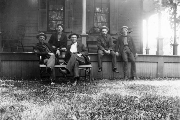 Group portrait of boarders, all railroad shop workers, sitting on the front porch at Mrs. Armour's boarding house. Left to right are: Bill Salsig, Roy Martin (donor of the photograph), Henry Perkins, Andy Taylor, and Guy Bruce.