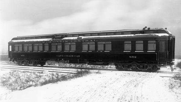 View from road of Wisconsin Central Railroad cafe-chair car No #852 sitting on railroad tracks at a crossing. Snow is on the ground.