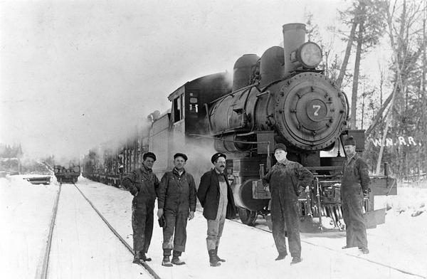 Engine #7 of the Wisconsin & Northern Railroad, which was purchased in 1917, seen here at Scott Siding, Wisconsin. The known railroad employees in the picture are, third from the left: conductor John Fowler and, on his right, engineer L.G. Guenther.