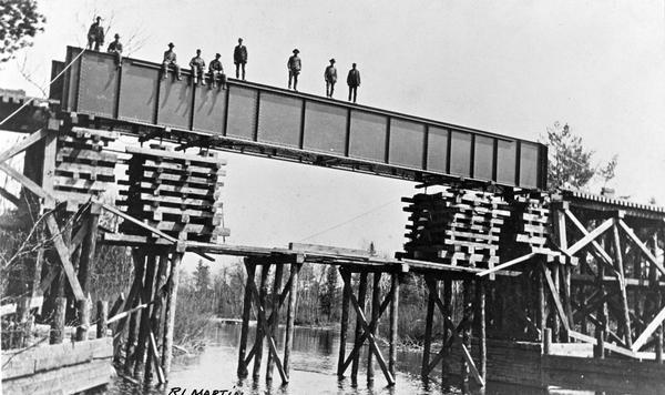 View from shoreline of men standing on the bridge over west branch of the Wolf River. They are constructing the Wisconsin & Northern railroad bridge.