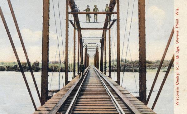Colorized view depicting the Wisconsin Central Railroad bridge at Stevens Point, with several men standing on top of the bridge painting the structure. Caption reads: "Wisconsin Central R. R. Bridge, Stevens Point, Wis."
