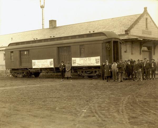 Group of people standing in front of a Soo Line freight car that was used by the railroad to promote hog transportation. This photograph was donated to the Historical Society by James Lyndon, a former public relations official with the Minneapolis, St. Paul, & Sault Ste. Marie Railway, who has identified the man on the far left as village president G.T. Vorland, a man interested in improving farming methods. Fourth from the left is E.C. Frost, a district official of the Soo Line, and sixth from the right is local farmer John Gunderson.