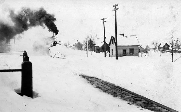 Winter scene of a snow-covered locomotive plowing its way through Barron, following a storm.