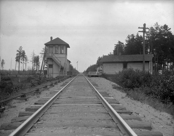 View down center of railroad tracks towards Holmes Junction, an intersection of the Wisconsin & Michigan and the Chicago, Milwaukee, & St. Paul railroads, three miles south of Pembine. Includes the interlocking tower, the station, the freight house, and the section foreman and agent's house. The junction was abandoned in 1918.