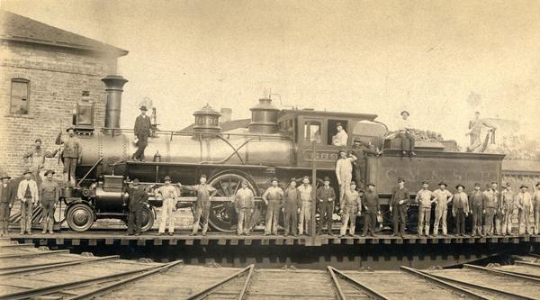 Chicago, Milwaukee, and St. Paul engine #689 on the turn table, surrounded by railroad employees. The pump house is in the background.