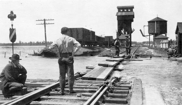 Four men inspecting the washout of Minneapolis, St. Paul and Sault Ste. Marie tracks caused by a flood at Medina Junction. The view is looking west from the old depot at the Chicago and North Western Railway crossing.