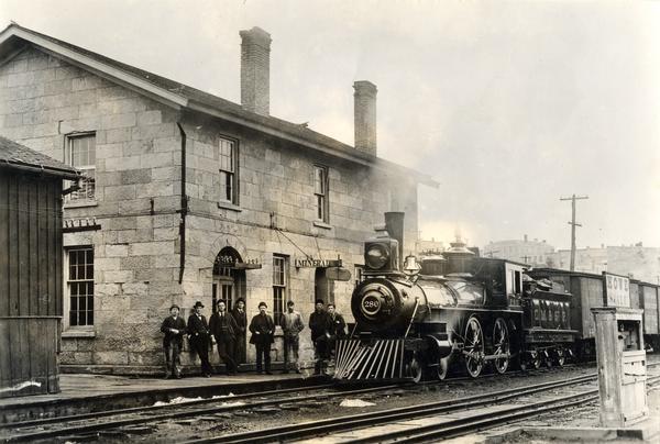 Chicago, Milwaukee and St. Paul Railroad locomotive #280 at the Mineral Point depot. A group of people stand on the platform. The depot was built in 1857, making it Wisconsin's oldest extant railroad depot.