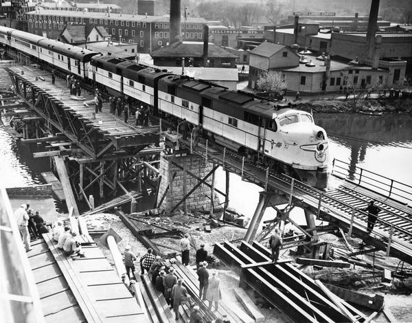 Elevated view of a Chicago and Northwestern passenger train, which is the first across a new bridge in Sheboygan. There is a group of people standing near the railroad train.