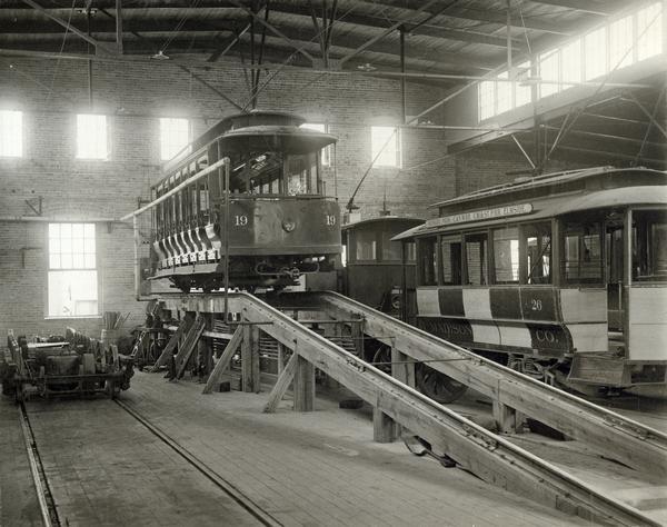 Interior view of the repair shop of the Madison Traction Company on Fair Oaks Avenue. An open streetcar is on the ramp, with a closed car from the Wingra Park-Elmside line and a second unidentified car nearby.