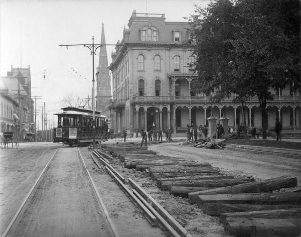 Construction of new streetcar tracks on the Capitol Square. In the background, on the corner of Main and Carroll streets, is the Park Hotel. Behind the hotel is St. Raphael's Catholic Church. On the right is a corner of the Capitol Park.