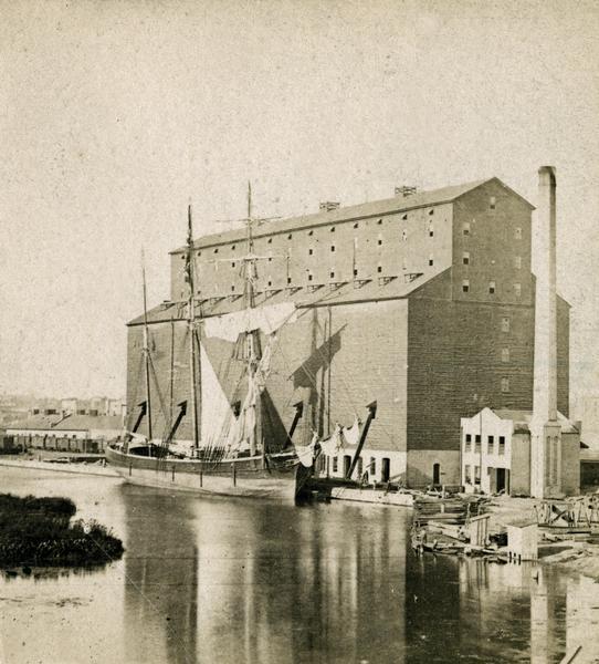 The Milwaukee & St. Paul Railway Company grain elevator at the Milwaukee harbor, with a sailing ship anchored nearby.