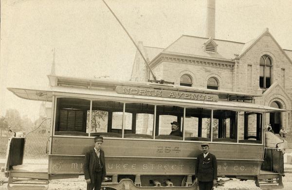 Streetcar #254 of the Milwaukee Street Railway Company on the North Avenue line, together with three company employees. Two men sit on the front steps of a large Romanesque building in the background.