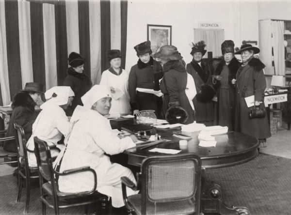 Volunteers signing up at the Red Cross office in New York to do hospital or other volunteer work. The woman in the white smock and dark hat is Mrs. Belmont Tiffany. Although this photograph is undated its caption indicates that it took place before the declaration of war.