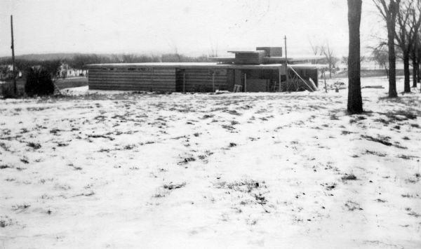 Side elevation of Herbert Jacobs Residence I, designed by Frank Lloyd Wright, during construction. There are open fields surrounding the structure. Construction began in 1936 or 1937, and is considered to be the first Usonian Home.
