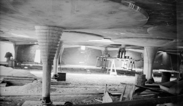 Tapered columns in the Johnson Wax Building during construction. Workmen are working on scaffolding built around one of the columns. The building was designed by Frank Lloyd Wright.