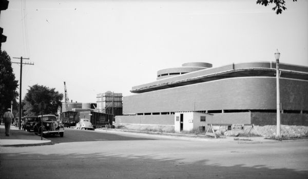 Rear elevation of the Johnson Wax Administration Building during construction. Construction sheds and a crane are visible on the building site. The building was designed by Frank Lloyd Wright.