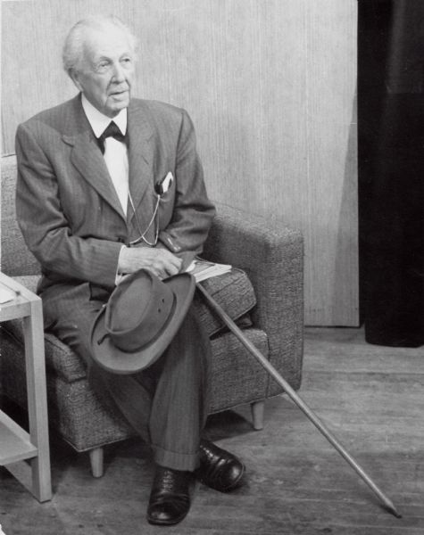 Frank Lloyd Wright seated in the WHA-TV studios. Wright is holding his hat and a walking stick.
