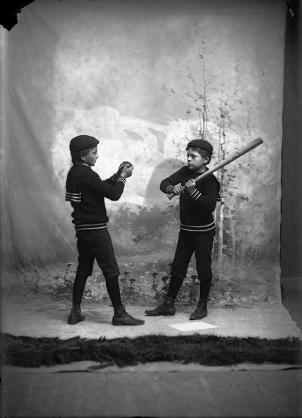 Studio portrait in front of a painted backdrop of two of the Gesell boys in a baseball pose.