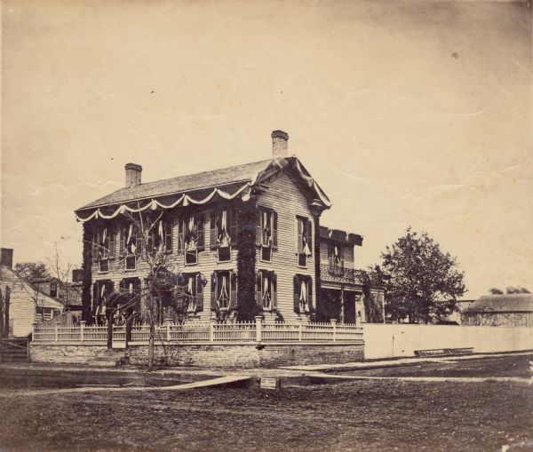 Albument print of the home of Abraham Lincoln decorated for Lincoln's funeral. The home is decorated with bunting across the roof and windows.