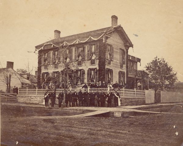 Albumen print of the Congressional Committee, in front of the Abraham Lincoln home for Lincoln's funeral. The Congressional Committee accompanied Lincoln's body all the way to Springfield. From time to time crowds around the Lincoln home would be cleared away for official photographs of mourners. The home is decorated with mourning ribbons.