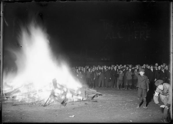 Large crowd gathered at University of Wisconsin bonfire, perhaps after a football game. Text "The gang's all here" is written on the negative.