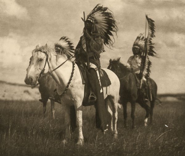 Three Plains Indians on horses with full headdresses.