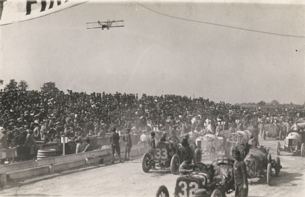 Photojournalist Fred Wagner covered the 1912 Milwaukee Grand Prize automobile race (later called the American Grand Prix) from Farnum Fish's airplane. The airplane is seen here flying over the racetrack, racecars and crowd.