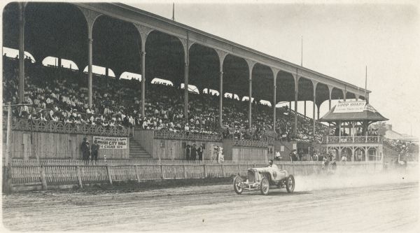 A solitary open car races past the grandstands at the Wisconsin State Fairgrounds.