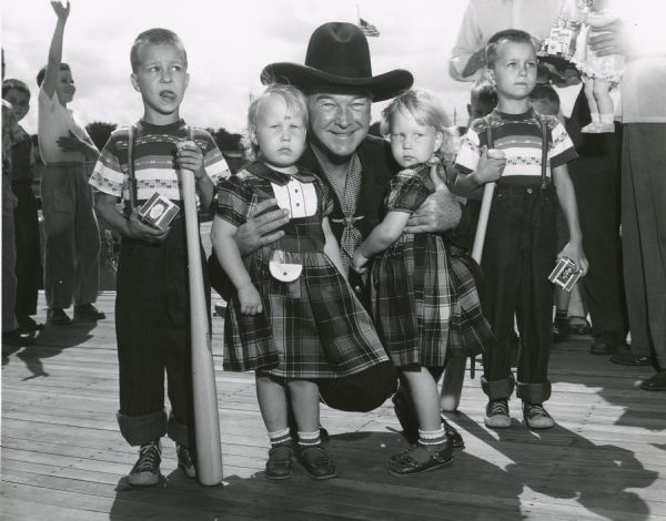 Actor William Boyd, better known as Hopalong Cassidy, with two pairs of twins entered in the twin competition at the Wisconsin State Fair. None of the children appear impressed by meeting the famous cowboy television star.