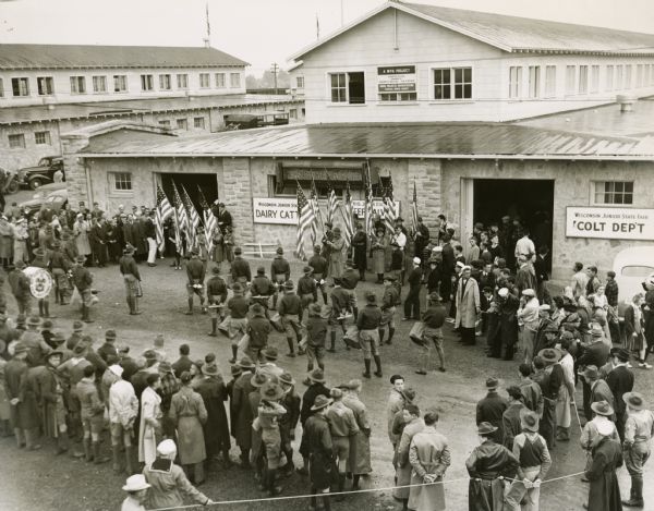 Elevated view of the dedication of the Junior Fair barn at the Wisconsin State Fair, the construction of which was a WPA project. A Scout band provides the music and makes up a large part of those in attendance.