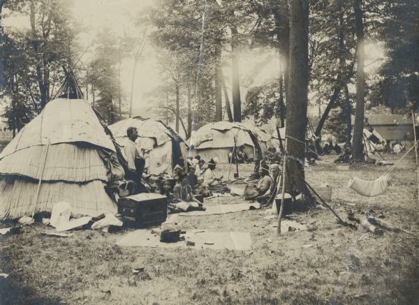 The Lac Courte Oreilles village sponsored by the Wisconsin Archaeological Society at the 1906 Wisconsin State Fair. Several members of the society are included in the picture and in the background is a building labeled "Gents' Toilet."