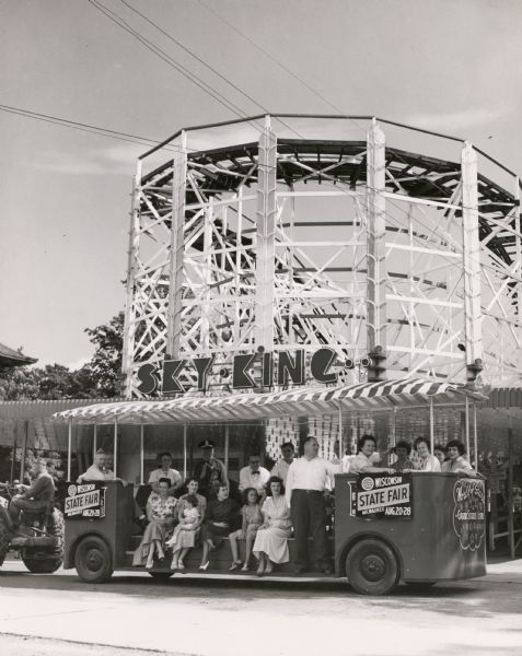 Fairgoers ride a tractor-drawn passenger wagon at the Fair. In the background is the Sky King roller coaster.