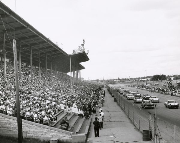 Automobiles drive past the grandstand at the Wisconsin State Fairgrounds as they prepare for the beginning of the race.