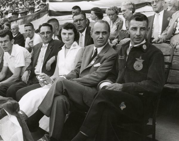 Governor Walter J. Kohler, Jr., sits in the grandstand at the Wisconsin State Fair with two FFA presidents: Joanne Salom of Chilton and Joe Conlin of Columbus. To their left is State Fair official Willis Freitag.