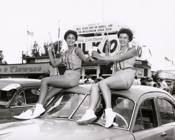Near the Department of Agriculture's Milk House, two baton twirlers in an obvious promotion photograph sit on top of a car and raise their paper cups of milk. For many years, baton twirling contests were a regular part of the annual fair schedule.
