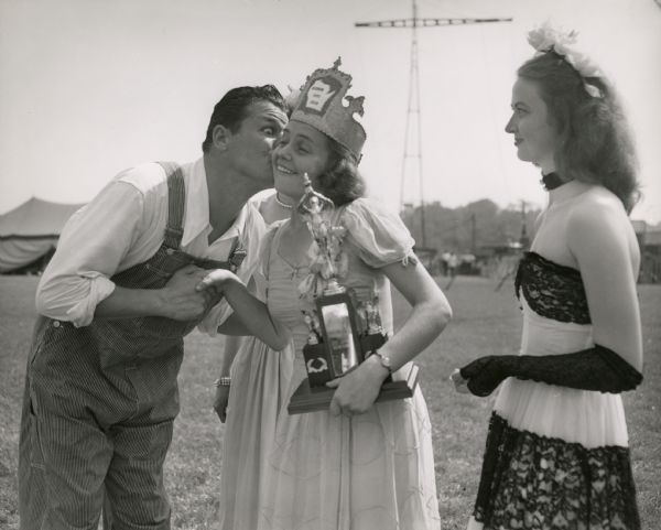 Actor Jack Carson congratulating the winner of the Wisconsin Dairy Queen at the Wisconsin State Fair, while another competitor is looking on.