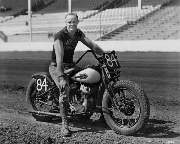 Bob Stuth, a motorcycle racer from Milwaukee, who competed at the Wisconsin State Fair. He is riding a Harley Davidson cycle and wearing a shirt that advertises that company's product.