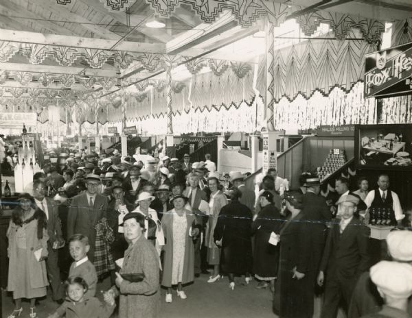 Interior view of the crowds in the Wisconsin Industry Building and the building's unusual art deco decoration. Few photographs depict African Americans at the State Fair, but careful observers will see a man and a woman on the left.