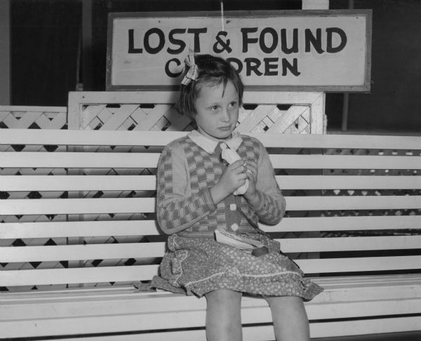 Margaret Mueller of Milwaukee, who had the distinction of being the first lost child at the Wisconsin State Fair. She is sitting in front of the sign that says "Lost & Found Children."