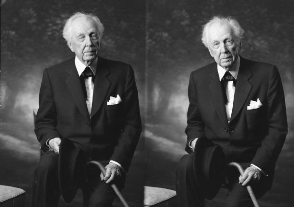 Two alternate views in front of a painted backdrop of Frank Lloyd Wright, seated, for an unretouched passport photograph. He is holding a cane in his left hand, and a hat in his right hand.