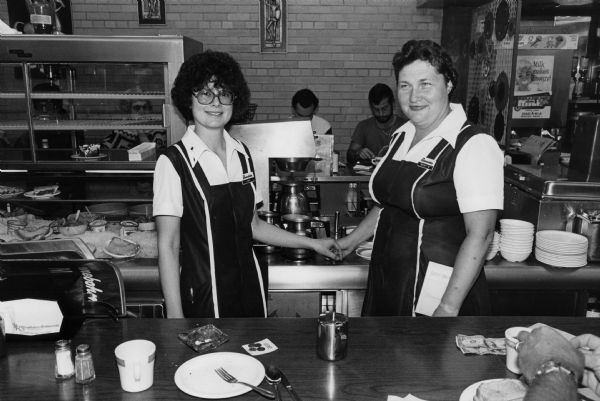 Joan and Mary S., two waitresses at the Rennebohm Drug Store No. 7 restaurant, 901 University Avenue, pose for the camera while standing behind the lunch counter.