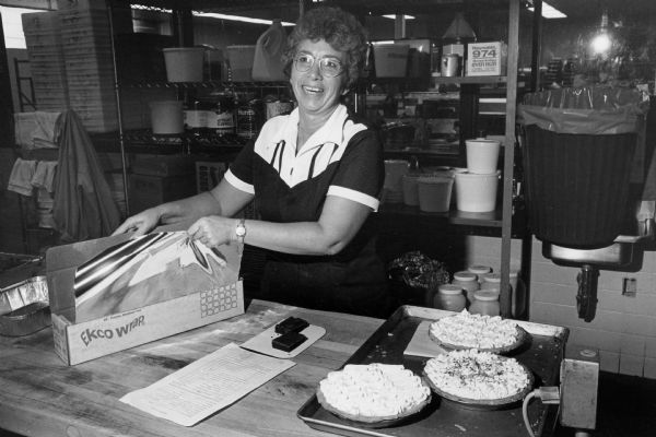 An unidentified Rennebohm Drug Stores, Inc., food service worker prepares to wrap three creme pies.